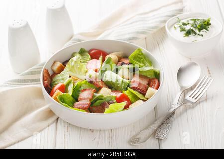 BLT-Salat mit Römersalat, knusprigem Speck, Tomaten, knusprigen Croutons und einem cremigen Knoblauchdressing auf dem Teller auf dem Tisch. Ge Stockfoto