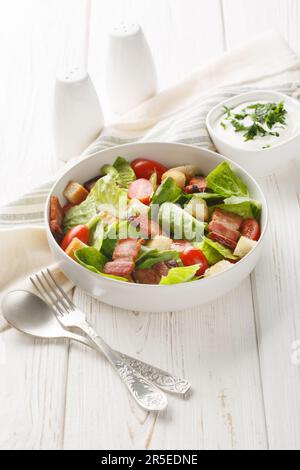 Der BLT-Salat wird mit frischem Salat, knusprigem Speck und hellen Tomaten, Croutons auf dem Teller auf dem Tisch gefüllt. Vertikal Stockfoto