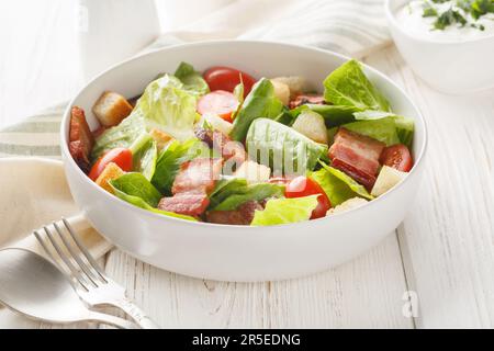 Gesunder BLT-Specksalat mit Salat und Tomaten auf dem Teller auf dem Tisch. Horizontal Stockfoto