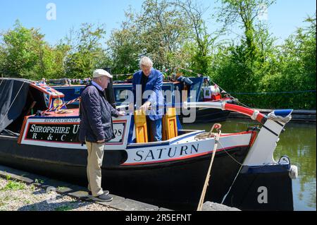 Zwei Männer unterhalten sich am Heck des Kanalboots Saturn, während es im Crickheath Basin am Montgomery Canal in Shropshire vor Anker liegt Stockfoto