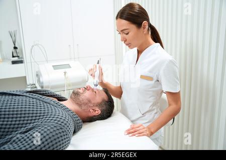 Weiblich in medizinischer Uniform führt RF-Hebevorgängen am Mann mittleren Alters durch Stockfoto