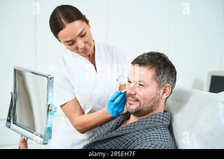 Der Mann sitzt vor einem Spiegel bei einer Beratung mit einem Kosmetiker Stockfoto