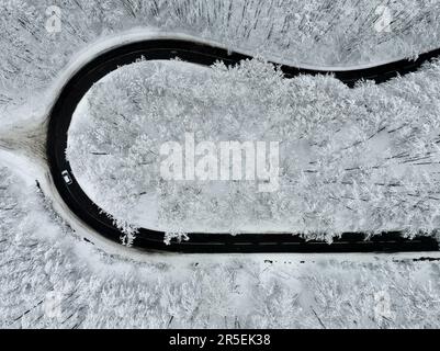 Kurvige Winterstraßen aus der Vogelperspektive. Diese Straße ist in einem Wald. Fantastische verschneite Landschaft von oben Stockfoto