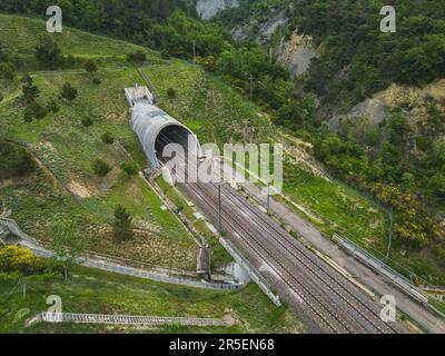 Luftaufnahme von Bahngleisen für Hochgeschwindigkeitszüge, die in einen Tunnel unter einem Berg fallen. Panoramablick auf die umliegenden Felder und Stockfoto