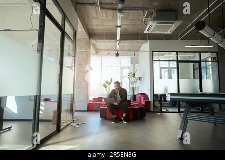 Ein hübscher Mann, der hart an einem Laptop arbeitet, in einem modernen Zimmer Stockfoto