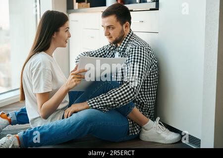 Glückliche lächelnde Ehepartner sitzen, umarmen und der Boden in der Küche Stockfoto