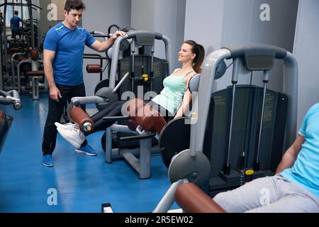 Eine lächelnde, fitte Dame, die Unterkörperübungen unter Aufsicht des Trainers durchführt Stockfoto