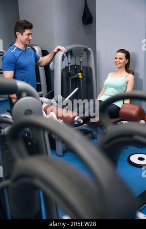 Eine freudige Frau, die unter Anleitung eines Sportlehrers ein Training am Unterkörper macht Stockfoto