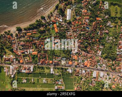 Die wunderschöne tropische Stadt liegt am Meer, umgeben von Bäumen und Hügeln. Die friedliche Szene hat einen blauen Himmel, flauschige Wolken und schimmerndes Wasser Stockfoto