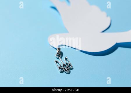 Anhänger mit ukrainischem Wappen und Papiertaube auf blauem Hintergrund, Nahaufnahme Stockfoto