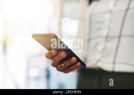 Vernetzt zu sein bedeutet, dass sie immer verfügbar ist, wenn ihre Kunden es brauchen. Nahaufnahme einer unbekannten Geschäftsfrau, die ein Handy in einem Büro benutzt. Stockfoto