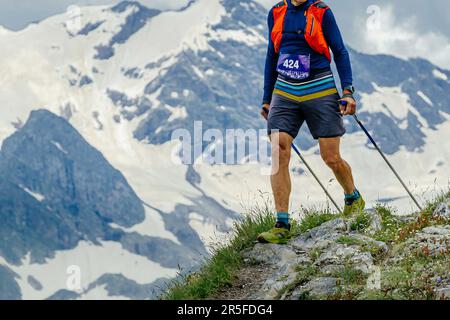 Ein Sportler läuft auf einem Marathon-Trail im Hintergrund in schneebedeckten Bergen, mit Stöcken in den Händen Stockfoto