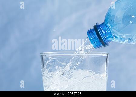 Aus dem Flaschenhals fließt frisches und kühles Wasser. Wasser wird aus einer Plastikflasche in ein Glas gegossen. Speicherplatz kopieren. Nahaufnahme Stockfoto