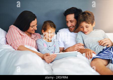 Wenn wir einander haben, haben wir alles. Eine junge Familie, die ein Tablet benutzt, während sie zu Hause im Bett zusammen chillt. Stockfoto