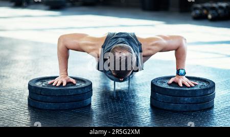 Die legale Art, fit zu werden. Ein junger Mann, der Liegestütze mit Gewichten in einem Fitnessstudio macht. Stockfoto