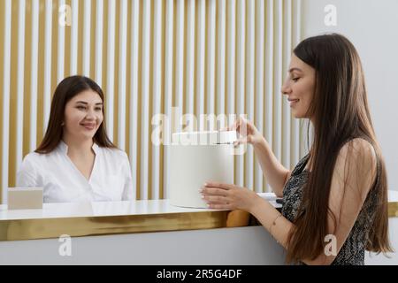 Weibliche Rezeptionistin an der Rezeption mit einem Kunden in einem modernen Büro. Ein komplementäres Gegenwartskonzept Stockfoto