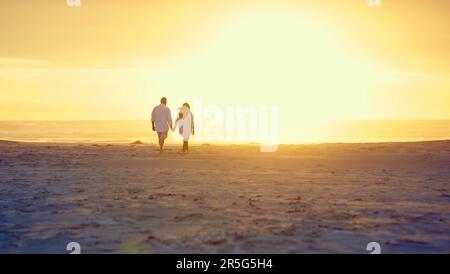 Hand in Hand am Strand. Rückblick auf ein liebevolles, reifes Paar, das Hand in Hand am Strand spaziert. Stockfoto