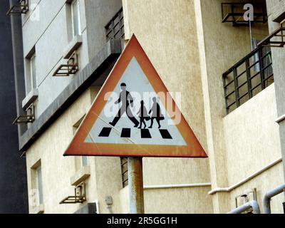 Ein Schild am Straßenrand, das die Fahrer auf Kinder aufmerksam macht, die die Straße überqueren, und Schulkinder, die vor dem Überqueren der Straße warnen Stockfoto