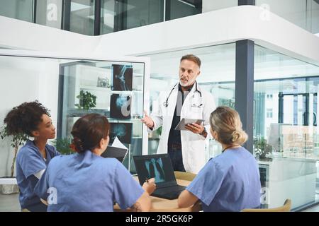 Testinterpretation mit seinem Team. Ein reifer Arzt, der ein Gespräch mit seinen Kollegen in einem Krankenhaus führt. Stockfoto