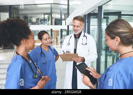 Jede Schwester hat ihren Posten. Ein gut aussehender, reifer Arzt, der mit seinen Krankenschwestern steht und ein Gespräch in der Klinik führt. Stockfoto