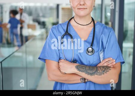 Wechselnde gesellschaftliche Sichtweise auf Tätowierungen in medizinischen Berufen. Eine unerkannte Krankenschwester, die tagsüber in der Klinik stand und ihre Arme verschränkte. Stockfoto