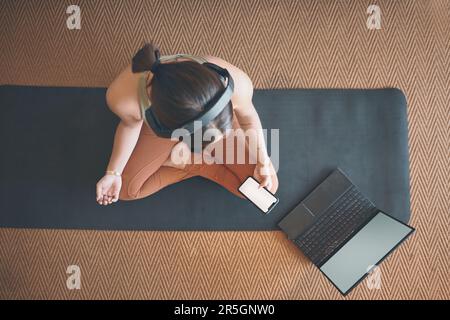 Ich lerne online von den Yoga-Meistern. Aufnahme einer jungen Frau mit Handy und Laptop, während sie zu Hause trainiert. Stockfoto