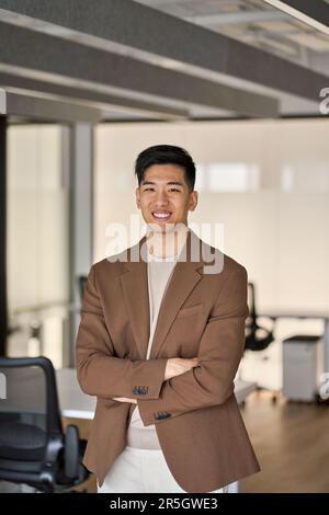 Junger, glücklicher asiatischer Geschäftsmann, der im Amt steht. Vertikales Hochformat. Stockfoto