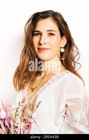 Modeporträt einer hübschen jungen Frau, die ein Kleid im Bogo-Stil trägt, einen Strauß trockener Blumen in der Hand hält, ein Hippie-Model, das auf weißem Hintergrund posiert Stockfoto