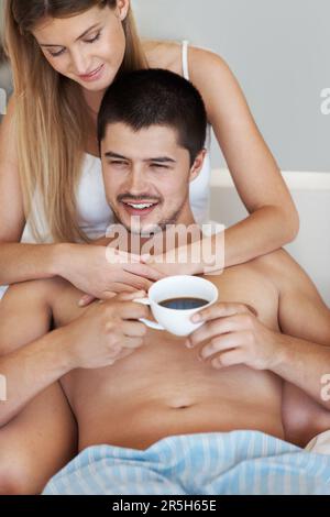 Ich genieße seinen Morgenkaffee. Ein gutaussehender junger Mann, der Kaffee im Bett genießt, während er sich mit seinem Partner entspannt. Stockfoto