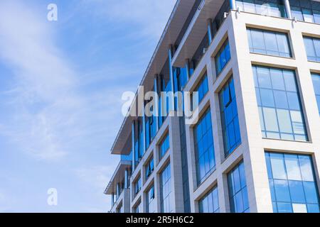 Stilvolle Glasfassade aus blau getöntem halbtransparentem Glasgebäude gegen den blauen Himmel mit Sonnenstrahlen. Modernes Architekturkonzept Stockfoto