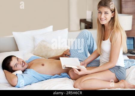 Neue Wege finden, Zeit miteinander zu verbringen. Junge Frau liest ihrem Partner vor, während sie sich im Bett entspannen. Stockfoto