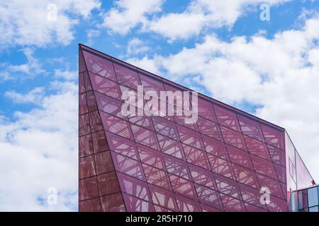 Stilvolle Glasfassade aus Violett getöntem, halbtransparentem Glasgebäude mit Sonnenstrahlen am blauen Himmel. Modernes Architekturkonzept Stockfoto