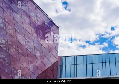 Stilvolle Glasfassade aus Violett getöntem, halbtransparentem Glasgebäude mit Sonnenstrahlen am blauen Himmel. Modernes Architekturkonzept Stockfoto