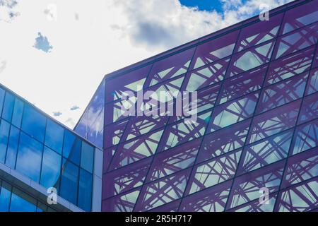 Stilvolle Glasfassade aus blau und violett getöntem, halbtransparentem Glasgebäude mit Sonnenstrahlen am blauen Himmel. Modernes Architekturkonzept Stockfoto