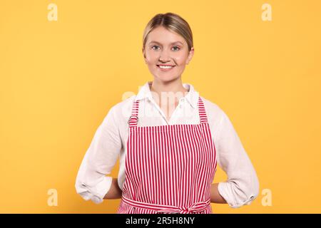 Wunderschöne junge Frau in einer sauberen gestreiften Schürze auf orangefarbenem Hintergrund Stockfoto