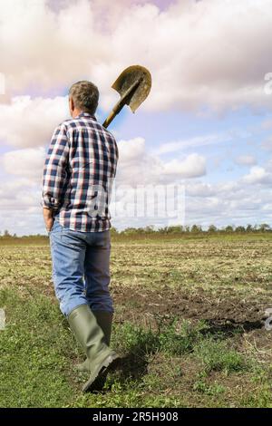 Mann hält Schaufel im Feld, Rückansicht. Grabvorgang Stockfoto