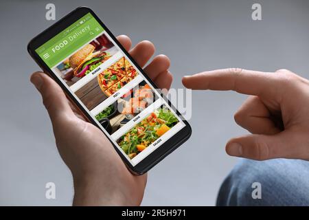 Lebensmittellieferservice. Mann wählt Gericht aus der Speisekarte vor Ort mit Smartphone auf hellgrauem Hintergrund, Nahaufnahme Stockfoto
