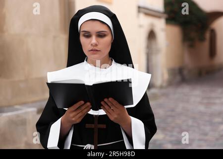 Junge Nonne liest Bibel in der Nähe von Gebäuden im Freien Stockfoto