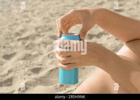 Frau öffnet Aluminiumdose mit Getränk auf Sand, Nahaufnahme Stockfoto