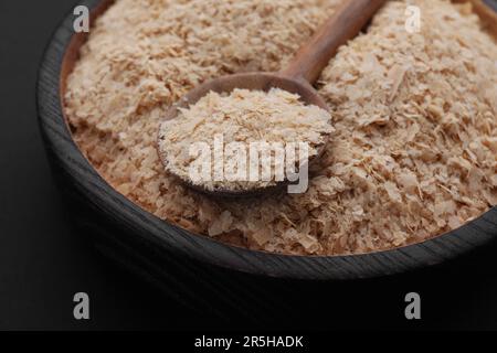 Schüssel und Löffel von Hefeflocken auf schwarzem Hintergrund, geschlossen Stockfoto