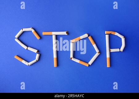 Word Stop aus Zigaretten auf blauem Hintergrund, flach liegend. Raucherentwöhnungskonzept Stockfoto