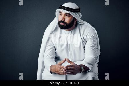 Traditionell, aber auch modern. Studiofoto eines jungen Mannes in islamischer traditioneller Kleidung, der vor einem dunklen Hintergrund posiert. Stockfoto