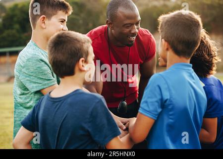 Sporttrainer, der sich mit seinem Grundschulteam trifft. Der Kursleiter führt ein Motivationsgespräch mit seinen Schülern auf einem Fachgebiet. Ein Mann, der eine Gruppe betreut Stockfoto