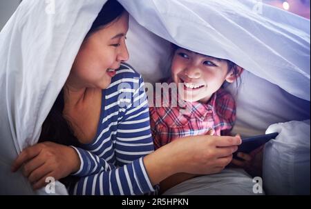 Es gibt nichts Schöneres als eine Mütterliebe. Eine attraktive junge Frau und ihre Tochter, die ein digitales Tablet benutzen, während sie unter der Decke liegen. Stockfoto