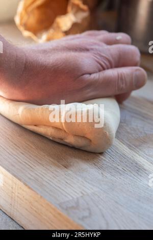Mann knete Teig auf einem Holzbrett. Teig ist eine hefefreie, flache Brotmischung Stockfoto