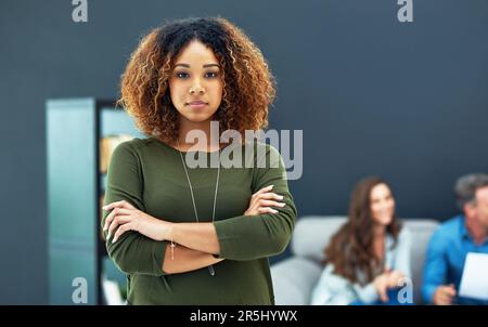 Wir engagieren uns voll und ganz für die Unternehmenskultur. Porträt einer selbstbewussten jungen Geschäftsfrau mit ihrem Team im Hintergrund verschwommen. Stockfoto