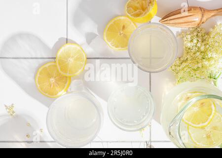 Sommererfrischungsmocktail mit Zitronen, Holunderblüten und Eiswürfeln in Gläsern auf weißem Hintergrund mit hartem Licht Stockfoto