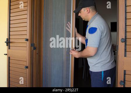 Bild eines Handwerkers, der eine Fliegengitter in einem französischen Fenster seines Hauses installiert. Schutz des Hauses vor Insekten. Stockfoto