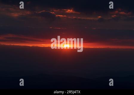 Sonnenaufgang mit dunklen Klumpen, Sonne und farbenfrohem Himmel vom Snetka-Hügel in den Krkonose-Bergen Stockfoto