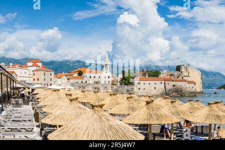 Die Altstadt von Budva wurde im Mai 2023 hinter Sonnenschirmen und Sonnenliegen am Wasser gesehen. Stockfoto